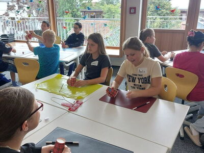 Schüler sitzen in Gruppen an Tischen und haben rot karierte Pappbecher in der Hand